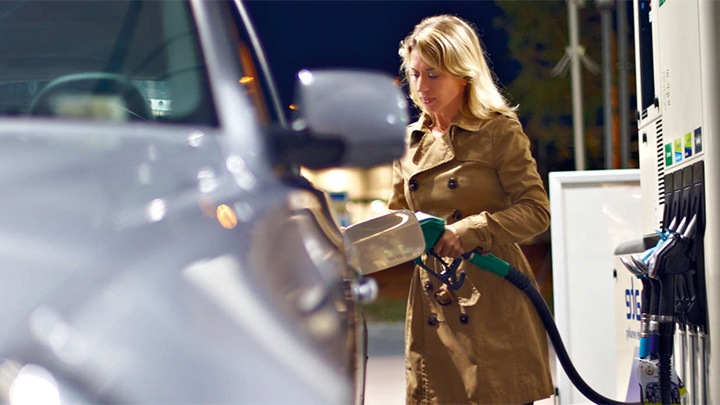 A woman fills her car’s tank at a gas station under the bright lights of Philips canopy lighting.